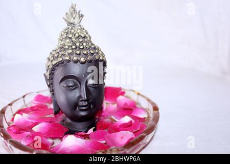 buddha dio faccia tra petali di rosa in ciotola, sfondo spa Foto Stock