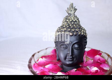 buddha dio faccia tra petali di rosa in ciotola, sfondo spa Foto Stock