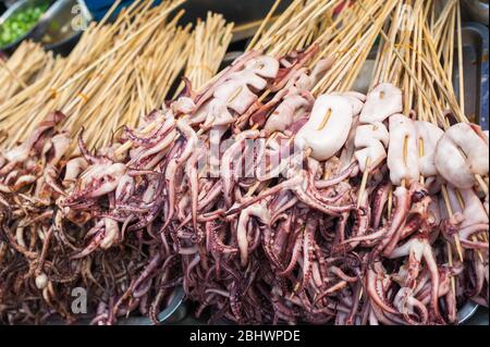 I spiedini di calamari si raccolgono in un mercato di strada a Luodai, Chengdu, provincia di Sichuan, Cina Foto Stock