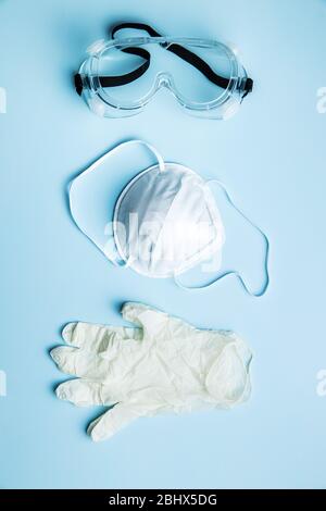 Occhiali di protezione, respiratore n95 e guanti. Dispositivi di protezione per coronavirus su sfondo blu. Vista dall'alto. Foto Stock