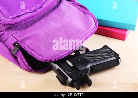 Pistola in zaino scuola su tavolo di legno, su sfondo luminoso Foto Stock