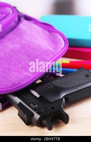 Pistola in zaino scuola su tavolo di legno, su sfondo luminoso Foto Stock