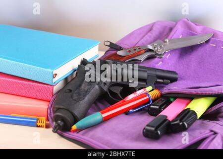 Pistola in zaino scuola su tavolo di legno, su sfondo luminoso Foto Stock