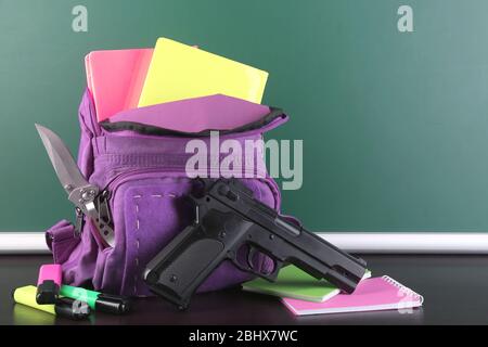 Pistola in zaino scuola su scrivania in legno, su sfondo lavagna Foto Stock