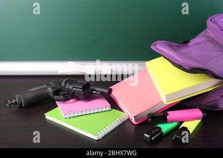 Pistola in zaino scuola su scrivania in legno, su sfondo lavagna Foto Stock