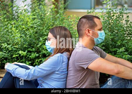 Giovane coppia con maschera protettiva seduta su panchina Foto Stock