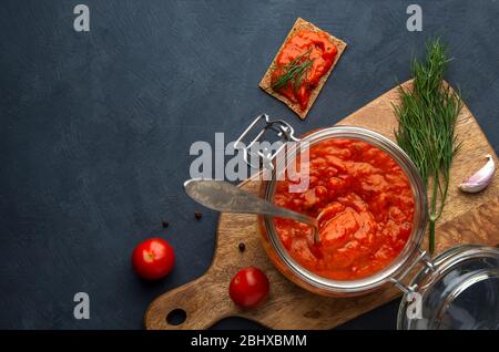 Cucina balcanica. Ajvar, pinjur, lutenitsa, harissa in riva su uno sfondo scuro. Vista superiore, spazio di copia. Foto Stock