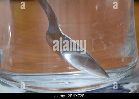 Cucchiaio di metallo in bicchiere di vetro vuoto. Macchie di calce cosparse di acqua sul vetro. Foto Stock