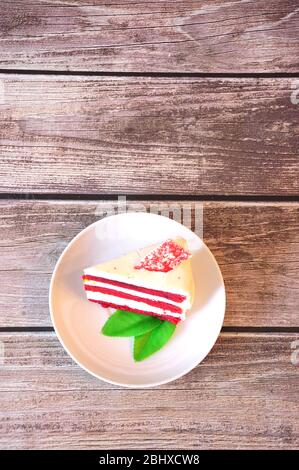 Un pezzo di cheesecake di velluto rosso decorato con foglie di menta su un piatto bianco si trova su un tavolo di legno. Primo piano. Foto Stock