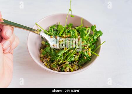 donna che mangia un'insalata fatta di germogli microgredi piselli e fagioli germogliati. cibo sano vegano Foto Stock