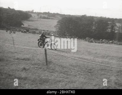 Anni '1950, storico, motoristico, uno scrambler sulla sua motocicletta, correndo lungo una collina erbosa, correndo fuori dagli spettatori, Inghilterra, Regno Unito. Foto Stock