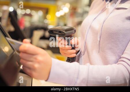 Giovane donna utilizza lo scanner per la scansione di merci su un POS per un cliente presso un enorme centro commerciale, concetto finanziario Foto Stock