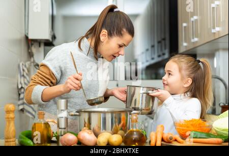 Felice giovane madre e piccola figlia assaggiando insieme zuppa di verdure Foto Stock