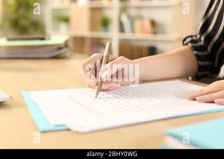 Primo piano delle mani della donna che compila il modulo di lavoro seduta su una scrivania a casa Foto Stock