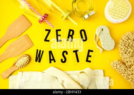 Concetto di zero sprechi. Sacchetti eco in tessuto, vasetti in vetro, spazzola e panno in legno per capelli e su sfondo giallo con testo nero Zero Waste al centro. Foto Stock