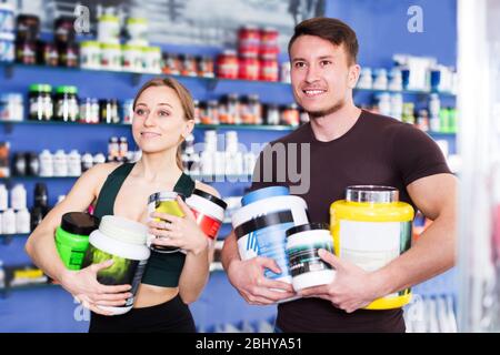 Sorridente fisicamente si adatta persone che tengono vaso di plastica di integratori alimentari sportivi all'interno del negozio Foto Stock