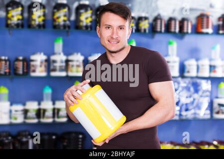 Fisicamente fit ragazzo che tiene vaso di plastica di integratori alimentari sport all'interno del negozio Foto Stock