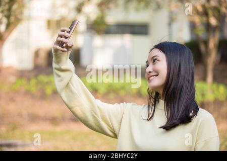 Le donne asiatiche cute stanno usando i loro telefoni per prendere selfie e sorridere felici nel giardino a casa. Foto Stock