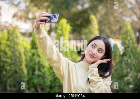 Le donne asiatiche cute stanno usando i loro telefoni per prendere selfie e sorridere felici nel giardino a casa. Foto Stock