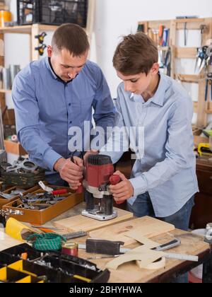 Felice unione falegname uomo e adolescente con asse di legno che lavorano in macchina emerying in officina Foto Stock