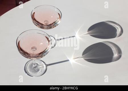 Due bicchieri di spumante sul tavolo rosa, alla luce del sole naturale e all'ombra. Foto Stock