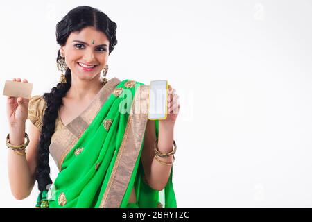 Giovane donna sorridente e con un telefono in mano e una carta di credito in un'altra. (Casalinga) Foto Stock