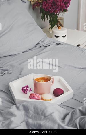 Vassoio con una tazza di caffè fresco e un dessert di macaron in piedi sul letto Foto Stock