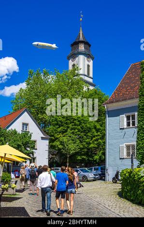 Scena urbana su Lingg Street con il campanile di Minster e la pubblicità zeppelin sopra la storica città vecchia di Lindau nel Lago di Costanza, Baviera, Germania. Foto Stock