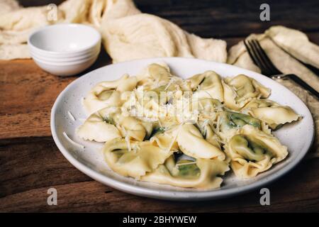 Ravioli italiani con spinaci, ricotta e parmigiano in cima, primo piano su un piatto. Stile rustico su tavolo in legno. Foto Stock
