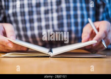 Uomo d'affari in camicia a mano che tiene la penna e le pagine di rotazione del notebook in ufficio a fuoco Foto Stock