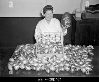 Le uova di Pasqua di cioccolato sono in grande richiesta quest'anno, ma l'offerta è molto limitata. Sono pochissimi i produttori che quest'anno stanno facendo a causa delle difficoltà razionistiche e della mancanza di potere umano. Una ragazza della fabbrica della navetta Worth gestisce alcune uova di austerità da due once, preparate per la corsa del nido della settimana. In una mano lei tiene un uovo di cioccolato pre-guerra per confronto solo per tormentare i compratori affamati. - Marzo 1947 Foto Stock