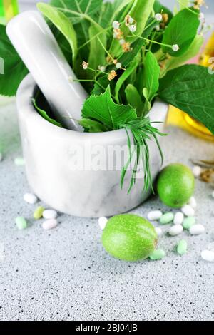 Erbe in mortaio, provette e pillole, su tavola, su sfondo chiaro Foto Stock