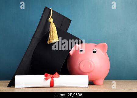 Piggy banca con cappello grad e diploma su sfondo lavagna Foto Stock