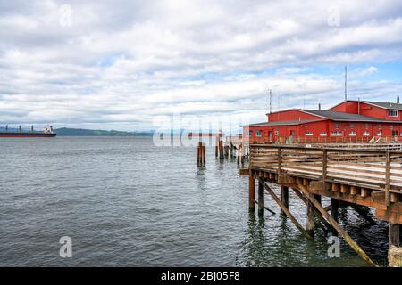 Rosso di edificio di legno sul vecchio molo pesca con pali di legno sporgente dall'acqua a bocca larga del fiume Columbia in Astoria city sulla Pacif Foto Stock