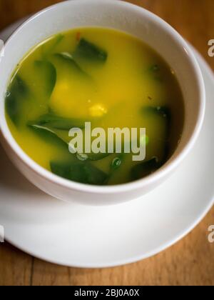 Zuppa fresca leggera a base di aragosta con zafferano, gamberi, piselli e foglie di spinaci serviti in una grande tazza di caffè. Foto Stock