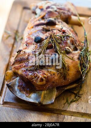 Spalla di agnello a tostatura lenta con aglio e rosmarino, su tavola di legno Foto Stock