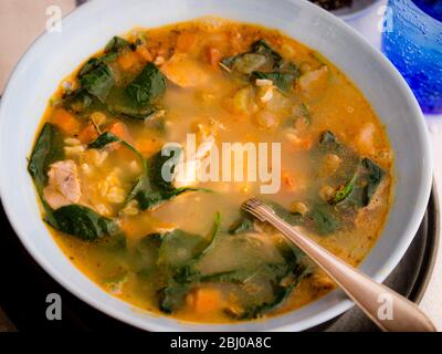 Un pasto completo la zuppa di pollo, il salame chorizo e verdure con riso marrone, Lenticchie e spinaci, servita in blu pallido ciotola Foto Stock