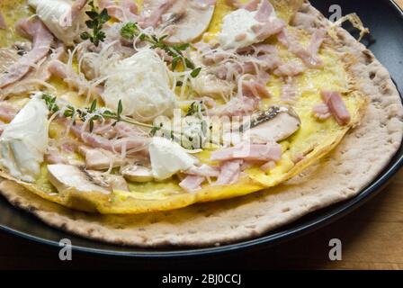 Frittata sottile con funghi, prosciutto, formaggio di capra e parmigiano su pane svedese prima di essere arrotolato, come colazione portatile. - Foto Stock