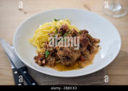 Sella di coniglio cotta al vino e al brodo, con scalogni, erbe e pomodori ciliegini, serviti con tagliatelle - Foto Stock