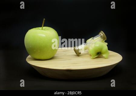 Mela verde, vetri di sabbia e anima di mela su un piatto di legno isolato su uno sfondo nero. Foto Stock