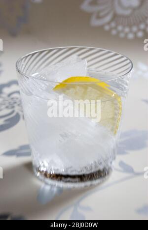 Vetro soffiato a spirale fine di spirito chiaro con soda o tonico, e fetta di limone su sfondo decorativo - Foto Stock