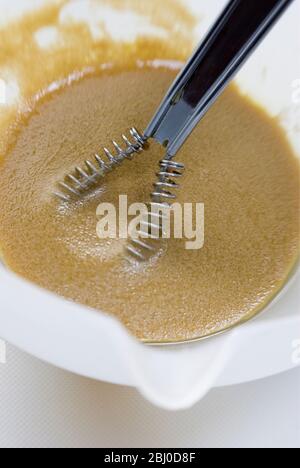 Preparazione di un classico condimento vinaigrette francese con senape, olio d'oliva e aceto di vino rosso, frittati insieme in una ciotola bianca - Foto Stock