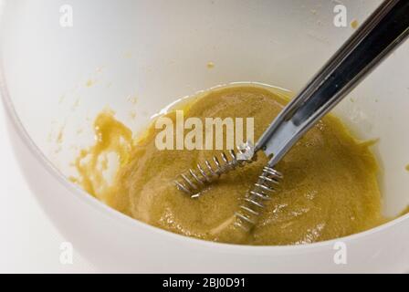 Preparazione di un classico condimento vinaigrette francese con senape, olio d'oliva e aceto di vino rosso, frittati insieme in una ciotola bianca - Foto Stock