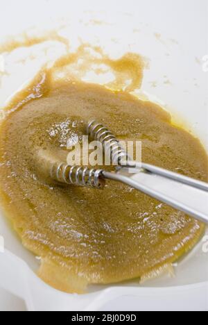 Preparazione di un classico condimento vinaigrette francese con senape, olio d'oliva e aceto di vino rosso, frittati insieme in una ciotola bianca - Foto Stock