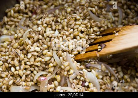 Cottura dei chicchi d'orzo con cipolle affettate in olio d'oliva, iniziando a fare risotto d'orzo - Foto Stock