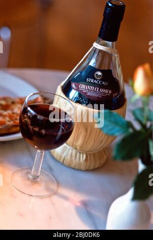 Chianti classico in tradizionale rafia coperta bottiglia di vecchio stile sul tavolo del ristorante con pizza - Foto Stock