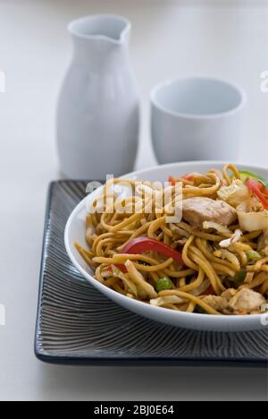 Spaghetti di ramen fritti con pezzi di pollo, peperoni rossi, germogli di fagioli, cipolle e carote e insaporiti con sosu, sale e pepe. - Foto Stock