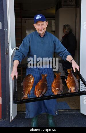 Uomo che tiene vassoio di salmone appena affumicato al pesce fumetto a Donsa, Svezia. Il salmone d'allevamento del fiordo norvegese è affumicato a freddo su trucioli di legno più ontano a poppa Foto Stock