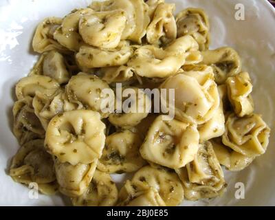 Primo piano di tortelloni cotti, insaccati in salsa di pesto su un piatto bianco - Foto Stock