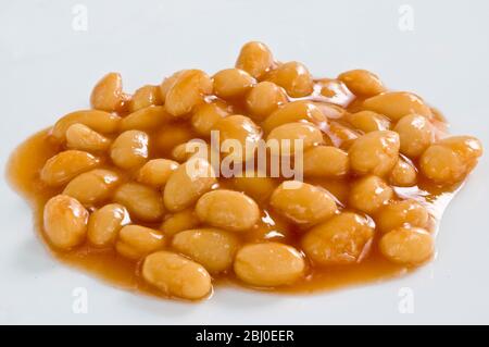 Piccolo mucchio di fagioli al forno in salsa di pomodoro su superficie bianca - Foto Stock